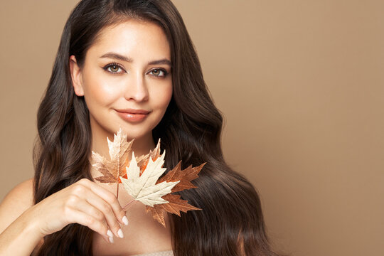 Portrait of beautiful young woman with autumn leaves. Healthy clean fresh skin natural make up. Long curly hairstyle. Care and beauty hair products
