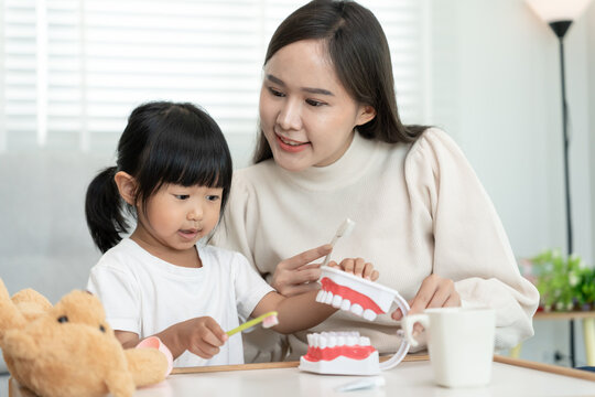 Mother teaching asian girl use toothbrush to clean, suffers from pain in tooth. Teeth decay, dental problems, tooth brushing practice, oral health care, reducing sweets, fluorine coating