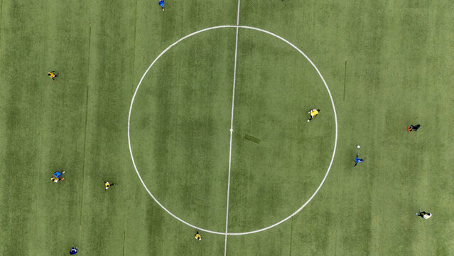 Aerial view of soccer players in yellow and blue jerseys competing on a green turf field with a white center circle in Lagos, Lagos, Nigeria.