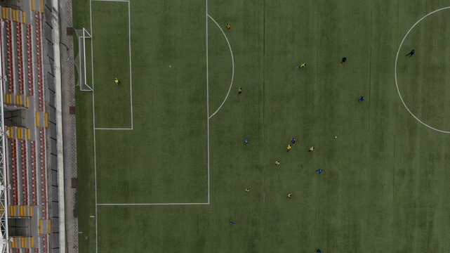 Aerial view of a soccer match in progress on a green field with players in yellow and blue jerseys, stadium seating visible on the side in Lagos Island, Lagos, Nigeria.