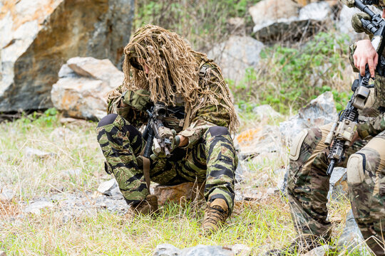 Soldiers in camouflage gear resting during training in a rocky outdoor area