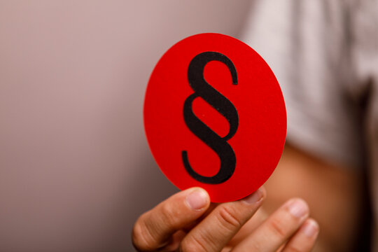 A hand holds a red card with a black paragraph symbol, representing law and justice.
