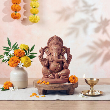 Ganesha statue with marigold flowers and small oil lamp on decorative stand
