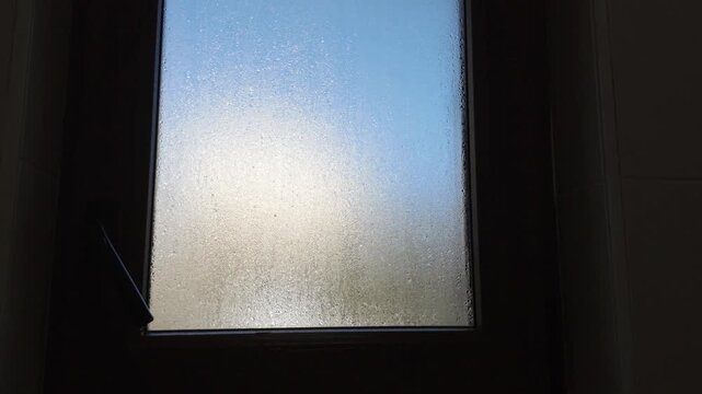 Very steamy bathroom window after hot showering, covered with condensation and water drops. Close-up view illustrating high humidity, moisture buildup, and reduced visibility on the glass.