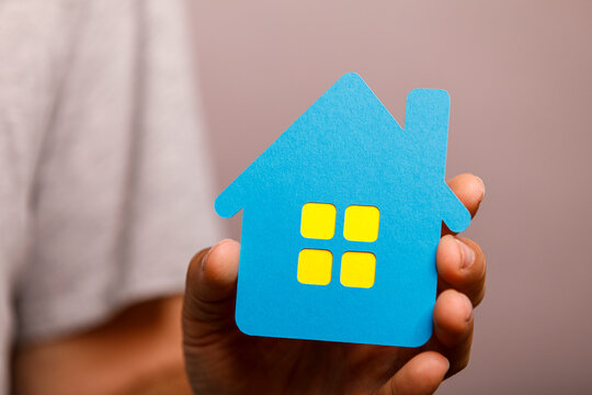 Symbolic blue house in hand, representing home, property, and real estate investment.
