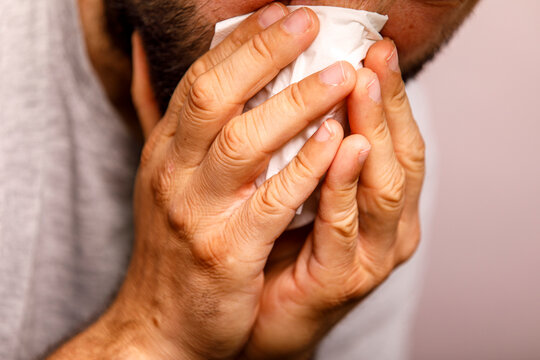 A man uses a tissue to blow his nose, suffering from cold, flu, or allergy symptoms.