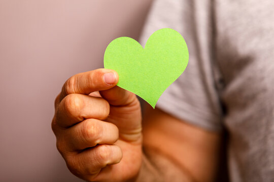 Close-up of a hand holding a green paper heart, representing love and environmental care.