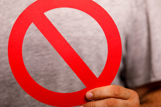 A person holds a clear red circular prohibition symbol, indicating stop or forbidden.