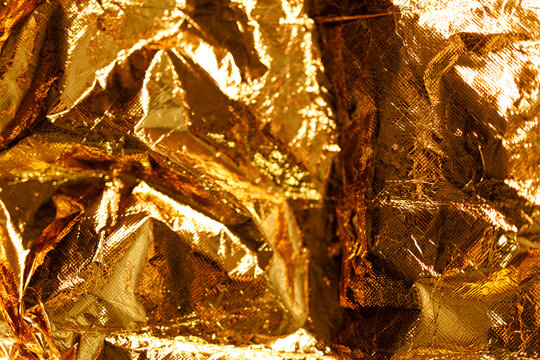 Abstract golden background featuring crumpled metallic foil with bright reflections.