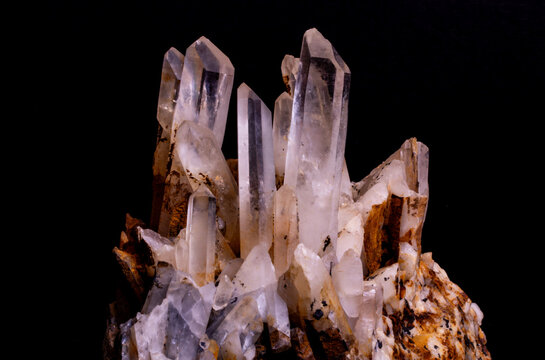Close-up studio shot of a translucent raw quartz crystal cluster showcasing sharp prismatic termination points against a stark black background.