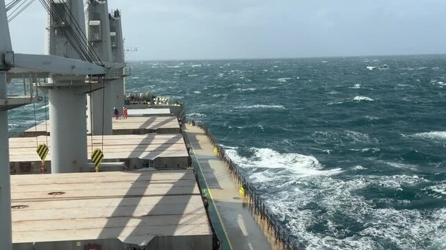 ship proceeding at rough sea crew working on hatch covers.