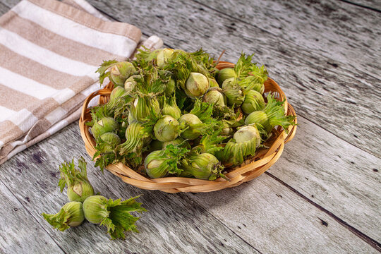 Fresh green cobnuts in woven basket on rustic wooden table with striped cloth background, natural lighting and shallow depth of field