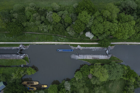 Aerial view of Hatton Locks on the Grand Union Canal with a narrowboat navigating the lock system, surrounded by lush green trees and vegetation in Hatton, England, United Kingdom.