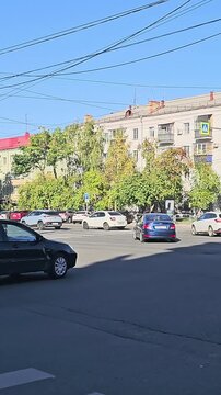 Urban street scene with cars and autumn trees. Blue SUV crosses intersection under clear sky. Pedestrians wait at crosswalk, unaware of traffic. Ideal for urban transportation or city life visuals