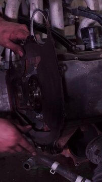 Close-up view of a mechanic hands working on car engine assembly, attaching a gasket and backplate in an auto repair garage.