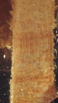 Macro shot of wooden texture on honey dipper submerged in sweet liquid. Great for food macro cinematography, natural products, and sweet recipes.