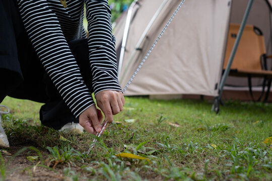 Camper securing a tent guyline to the ground at a campsite, preparing outdoor shelter for a camping adventure while enjoying nature, practical skills, recreation, and wilderness travel.