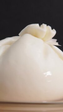 Vertical close up shot of soft burrata cheese pouch resting on plate side view.
