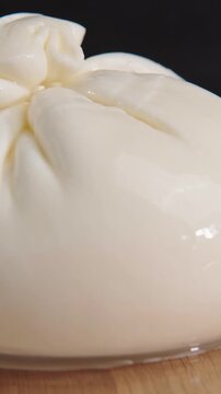 Vertical macro video of fresh white burrata cheese pouch rotating on wooden surface.