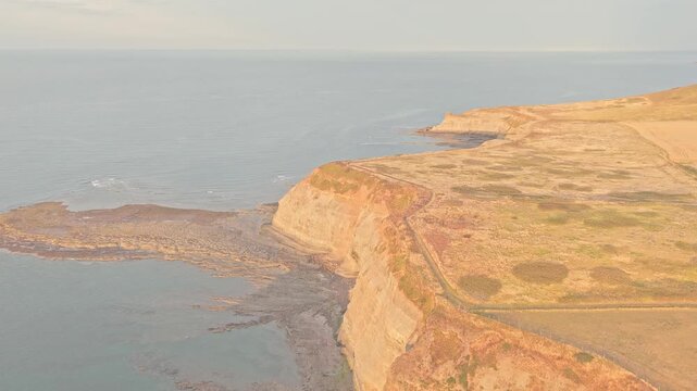 Staithes Coast extends along high Jurassic cliffs above the North Sea, with rocky shoreline, agricultural fields and coastal grassland across the headland, drone forward flyover