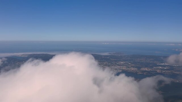 Cockpit view of El Ferrol city, in Spain, taken from an airplane cockpit, with the city emerging bellow some clouds in a blue sky.