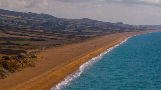 Aerial view of the coastline at West Bay with golden sandy beach, turquoise sea, and rolling green hills of the Jurassic Coast in West Bay, England, United Kingdom.
