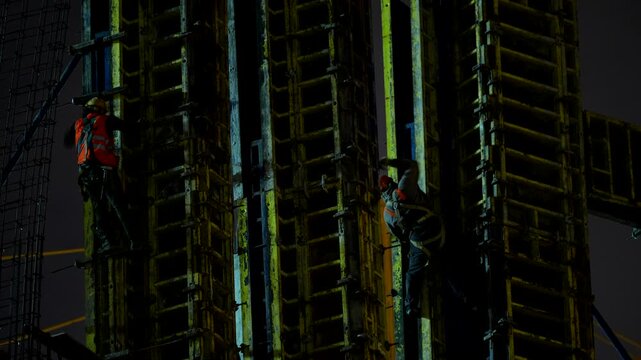 Workers installing formwork on a high rise concrete building at night, showing construction processes, engineering, safety and work at height