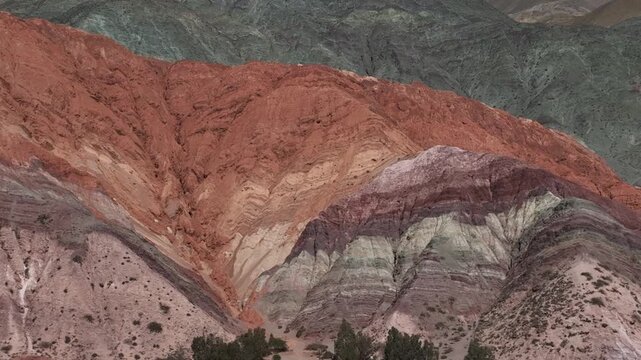 Aerial view of a massive red rock formation with the village of Purmamarca in the background, Jujuy. The Hill of Seven Colors draws tourists to this village in northern Argentina.