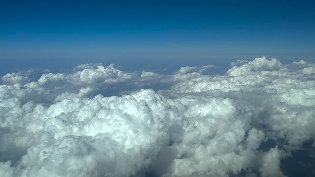 Cockpit view taken at cruise while flying at 13000 m high in the Stratosphere over towering storm cumulonimbus clouds under a blue sky.