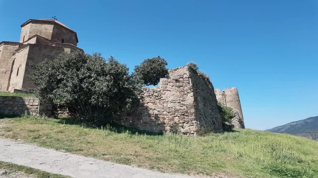 Historic Jvari Monastery surrounded by ancient stone walls and mountain landscape near Mtskheta, Georgia under a clear blue sky. Jvari Monastery and Ancient Stone Ruins in Georgia