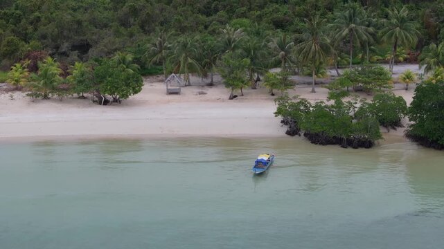 Aerial view of a small boat anchored near a sandy beach with palm trees and lush vegetation on Batam Island in Batam, Riau Islands, Indonesia.