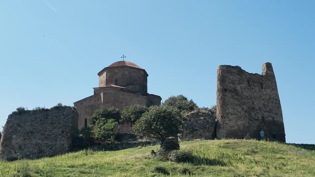 Video view of Jvari Monastery and weathered stone fortress walls on a hill above Mtskheta, Georgia, surrounded by green landscape under a clear blue sky. Jvari Monastery with Ancient Stone Fortress Ru