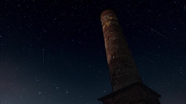 Time lapse of night sky full of falling meteors and rotating stars against tower building with. Dark black aerial scene with celestial particles ejected by comet leaving bright trails. Astronomy theme