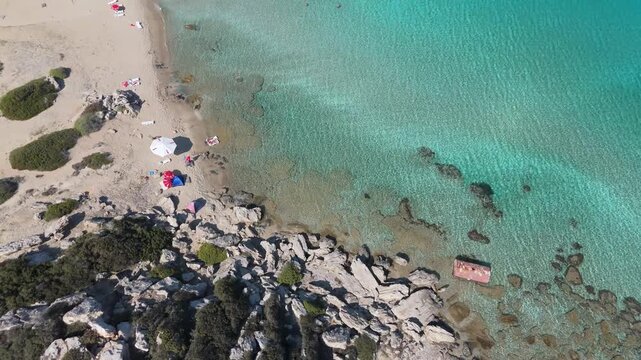 Aerial view of rocky coastline meeting turquoise Mediterranean waters with a small sandy beach and sparse vegetation in Famagusta, Famagusta, Northern Cyprus.
