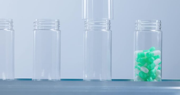 Slow motion green and white capsules dropping into clear plastic bottles on sterile pharmaceutical production line.