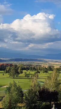 Scenic Golf Course Landscape with Rolling Greens, Trees and Distant Mountains Under Dramatic Clouds