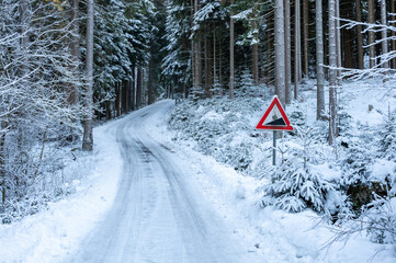 Obraz premium Road sign warning of a steep incline beside an icy and snow covered road in a winter landscape, highlighting hazardous driving conditions.