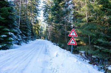 Obraz premium Road sign warning of slippery conditions beside an icy and snow-covered road in a winter landscape, highlighting hazardous driving conditions.