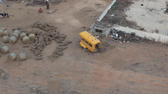 Aerial view of a yellow bus shell abandoned in a dusty field with hay bales and a cow in Famagusta, Famagusta, Northern Cyprus.