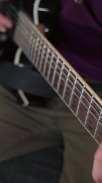 Vertical close up shot of a guitarist's right hand fingerpicking strings near the bridge pickup on an electric guitar.