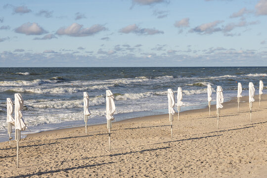 Closed beach umbrellas on sandy shore by rough sea with waves in daylight