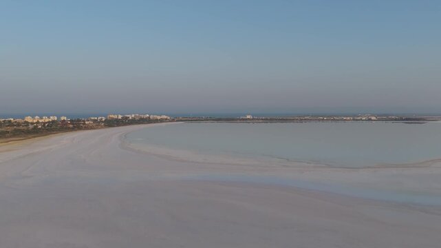 Aerial view of the expansive Larnaca Salt Lake with its calm, reflective surface and the distant cityscape of Larnaca, Larnaca, Cyprus.