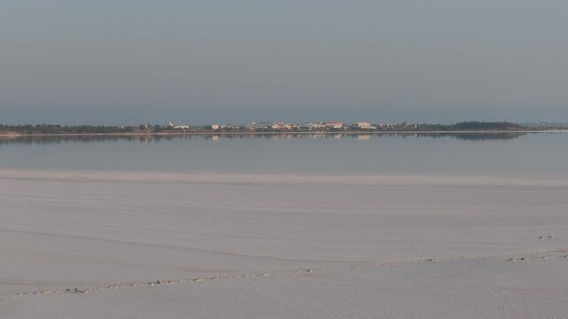 Aerial view of Larnaca Salt Lake with calm reflective water and distant buildings under a clear sky in Larnaca, Larnaca, Cyprus.