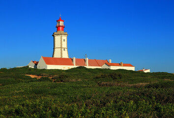 Portugal, Sesimbra. The emblematic, historic lighthouse at Cape Espichel, built in 1870 stands on a huge cliff on the Portuguese West Coast. Clear blue sky - Copy space. © john copland