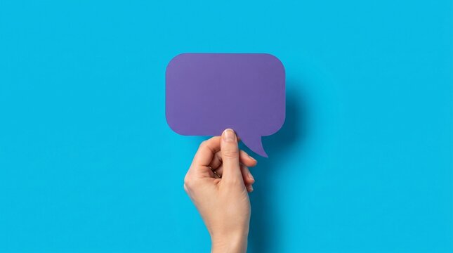 Human hand holding vibrant purple paper speech bubble cutout against vivid blue solid background presenting creative communication concept photography with minimalist studio lighting