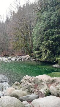 Clear emerald green pool of water surrounded by granite boulders and pine forest at Lynn Canyon in Vancouver, showing a tranquil natural swimming hole.