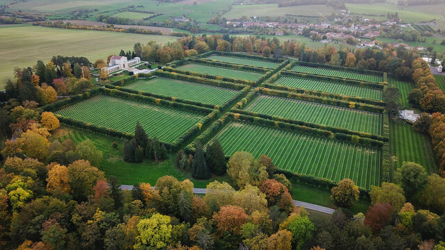 Aerial view of the World War 1 Meuse-Argonne American Cemetery and Memorial, with rows of white grave markers in manicured lawns and autumn trees in Romagne-sous-Montfaucon, Grand Est, France.