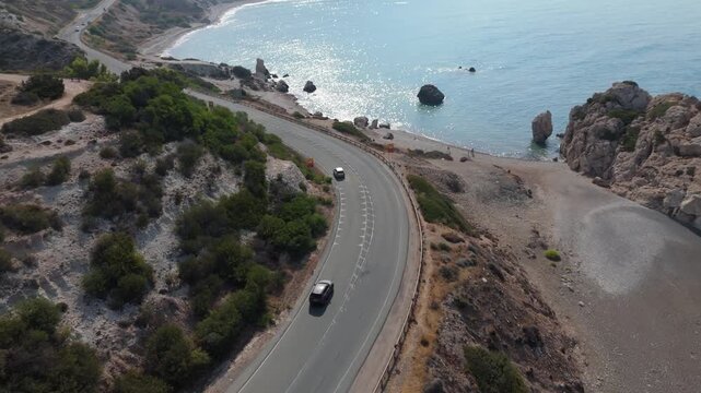 Aerial view of a car driving along the winding coastal road near Aphrodite's Rock with turquoise sea and rocky cliffs in Paphos, Paphos, Cyprus.