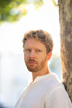 Man leaning against a tree with sunlight in the background during an outdoor setting