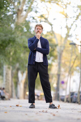 Fototapeta premium Man standing on a tree-lined street during the late afternoon with hands near his mouth